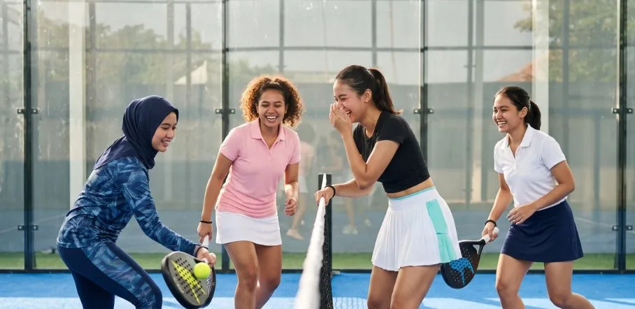 Four women laughing on a padel court